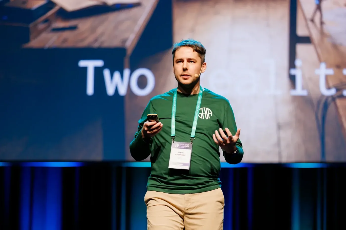 Speaker with a headset microphone in front of a large screen on a conference stage